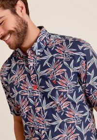 Korte mouw knoopshirt van navy stof met een rood en groen bladerenpatroon, met contrasterende rode knopen en een klein logo.