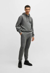 Grijze hoodie met koordjes en kangoeroezak, gecombineerd met bijpassende joggingsbroek. Glad materiaal, slanke pasvorm en ribgebreide manchetten.