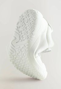 Sneaker blanche avec une tige texturée et une semelle en caoutchouc présentant un motif de semelle géométrique. Sangle réglable et talon rembourré pour le confort.