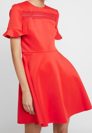 Robe rouge en tissu lisse, dotée de manches courtes à volants, d'un corsage ajusté et d'une jupe évasée avec des coutures décoratives au niveau du décolleté.