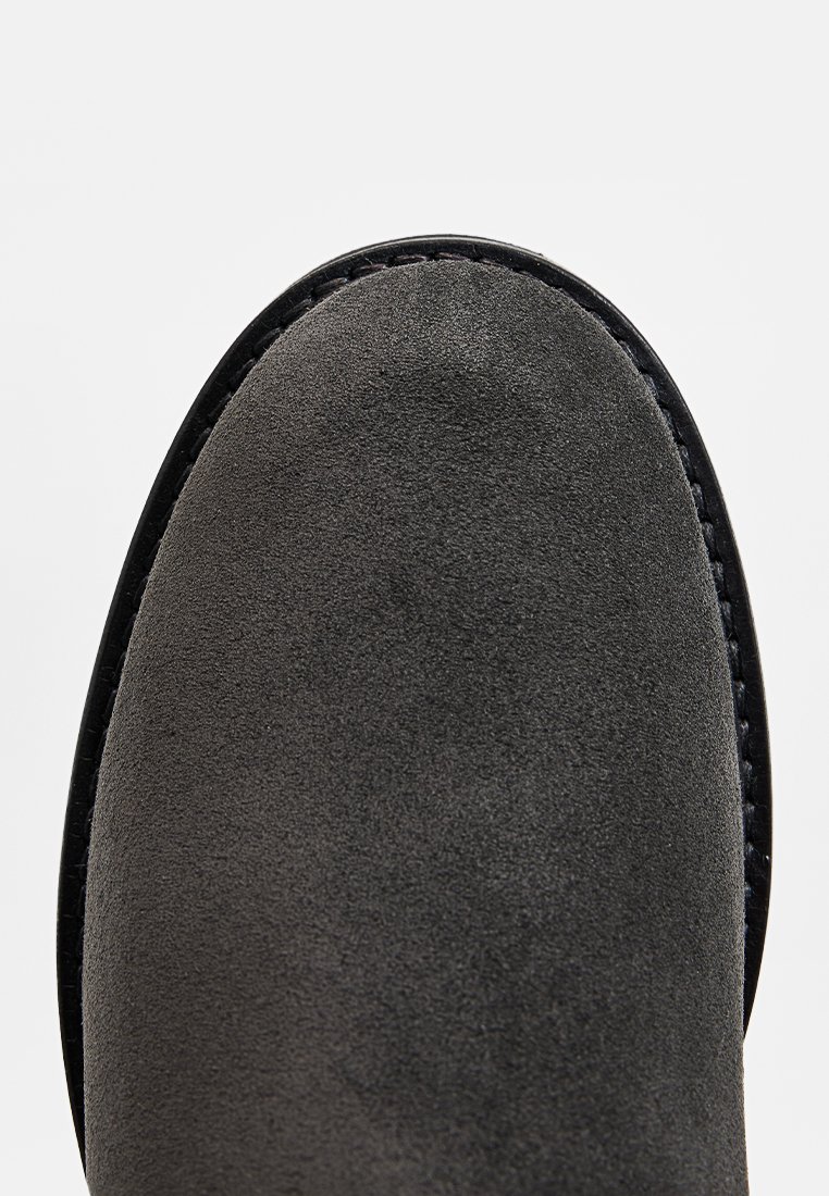 Szare zamszowe botki za kostkę z zaokrąglonym noskiem, czarnym szwem wzdłuż krawędzi i gładką fakturą, umieszczone na białym tle.
