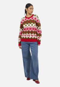 Maglione a maglia con motivi geometrici rossi, verdi e rosa; presenta alberi, fiocchi e fiocchi di neve; scollo rotondo; polsini e orlo a coste.