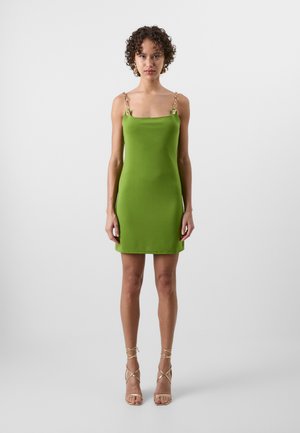 Groene mini-jurk met een vierkante halslijn, kettingdecoratie op de bandjes en een aansluitende silhouet. Gladde stof, kniehoogte, gedragen met bandjeshakken.