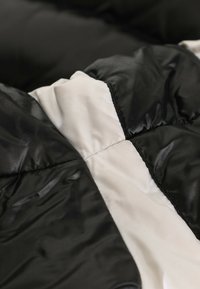 Gros plan d’un tissu matelassé noir et blanc avec une texture lisse, brillante et des lignes de couture visibles.