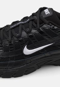 Baskets Nike en maille noire et cuir, présentant un swoosh blanc, des détails texturés et une conception de semelle durable.