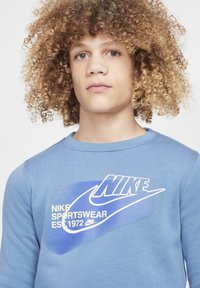 Sudadera de manga larga azul con un logo de Nike en blanco y texto en el frente. Hecha de material suave con un diseño de cuello redondo.