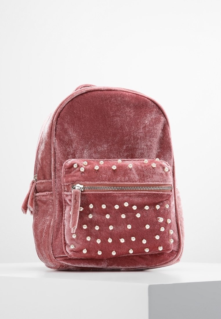 Rosa Samt-Rucksack mit abgerundetem oberen Teil, vorderer Reißverschlusstasche verziert mit weißen Perlen und plüschiger Textur. Verfügt über Seitentaschen und verstellbare Träger.