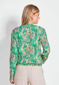 Groene bloemenprintjas met lange mouwen, een gathered taille en elastische manchetten. Heeft kleurrijke bloemenpatronen en een lichtgewicht stof.