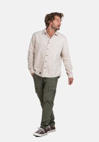 Helle beige Button-Up-Hemd, grüne Cargo-Hosen mit Taschen und braune Sneakers. Lockerer Schnitt, weicher Stoff und lässiger Stil.