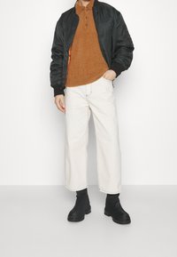 Svart bomberjacka, brun fluffig polo, vida vita byxor och svarta ankelstövlar. Släta texturer med kontrasterande färger.