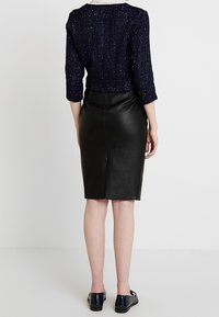 Námořnický pletený svetr s tříčtvrtečními rukávy v kombinaci s přiléhavou černou koženou sukní. Hladká textura a čistý silueta, minimální detaily.