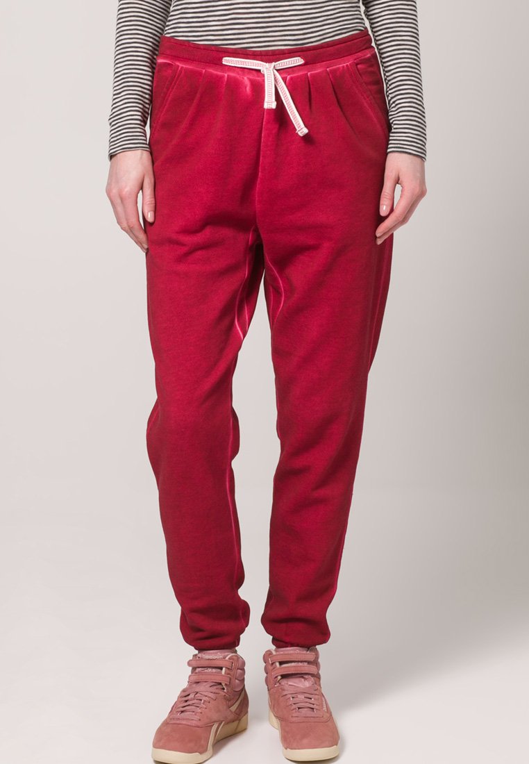 Sarkani sporta bikses ar elastīgu jostu un auklu, kurām ir sānu kabatas un brīva piegriezuma, papildinātas ar rozā kedām.