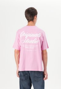 Lyserød t-shirt med korte ærmer og afslappet pasform. Har hvid grafisk tekst på ryggen og en glat bomuldsstruktur.
