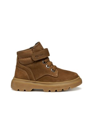 Bottines en daim marron avec une semelle en caoutchouc, dotées d'œillets en métal, d'une sangle Velcro et de détails de couture contrastants.