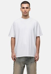 Witte oversized t-shirt van katoen, met een ronde halslijn en korte mouwen, tegen een effen achtergrond.