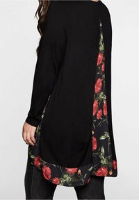 Zwarte lange mouwen top met een bloemenprintpaneel in rood en groen op de achterkant en langs de zoom, met een gebogen snit en zachte textuur.