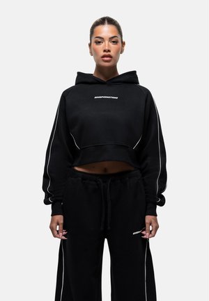 Felpa cropped nera con cappuccio e cordino, dotata di piping bianco e la scritta "GOODFORMNOTHING". Abbinata a pantaloni della tuta neri coordinati.