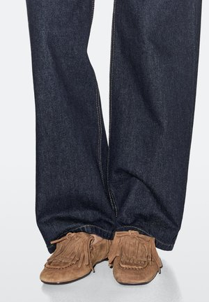 Dark blue denim jeans with a straight fit, paired with light brown suede moccasin shoes featuring fringe and bow accents.