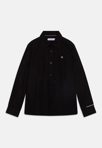 Svart skjorta med knappar, långa ärmar, spetstålig krage och CK-logga på bröstet. Har en slät textur och rät fåll.