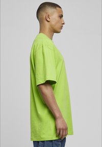 Helles grünes, übergroßes T-Shirt aus Baumwolle, mit lässigem Schnitt, kurzen Ärmeln und Rundhalsausschnitt. Glatte Textur, minimalistisches Design.