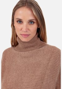 Pull à col roulé côtelé marron clair avec une texture douce, doté d'un col haut et d'une coupe décontractée, idéal pour superposer par temps frais.