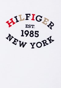 Bijela pamučna majica s ispisanim zakrivljenim logotipom u crnoj, crvenoj i bež boji: "HILFIGER EST. 1985 NEW YORK."
