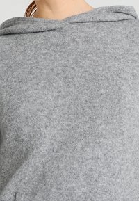 Sweat à capuche en tricot gris avec une texture douce, présentant une coupe décontractée et une capuche à cordon. Aucun motif ou détail matériel visible.