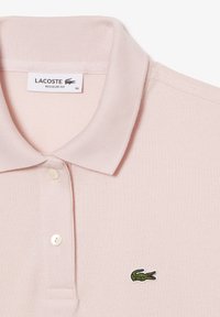 Ljusrosa polo shirt med en strukturerad tygkvalitet, utrustad med en klassisk krage, tre knappar och en liten grön krokodil-logotyp på bröstet.