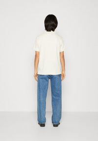 White short-sleeve polo shirt with textured fabric, paired with loose blue jeans. View from the back, showcasing simplicity and casual style.