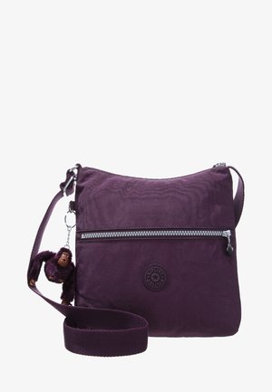 Sac bandoulière violet avec poche zippée à l'avant et porte-clés peluche singe attaché à la sangle réglable.