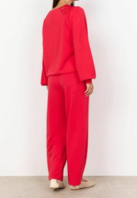 Conjunto de loungewear de algodón rojo que presenta un corte relajado, mangas anchas y detalles de encaje en la parte posterior. Los pantalones tienen una silueta holgada.