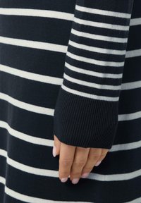 Marineblau und weiß gestreifter Strickpullover mit gerippten Bündchen. Verfügt über horizontale Streifen und eine weiche Textur. Nahaufnahme des Ärmels und der Hand.