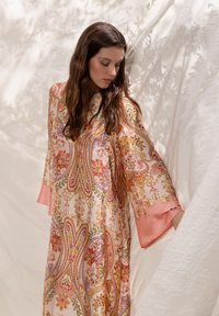 Longue caftan fluide en tissu doux à motifs aux tons pastel rose, or et couleurs vives, avec de larges manches et un col rond.
