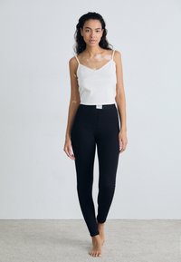 Black leggings with a fitted design and smooth texture, paired with a white ribbed tank top featuring thin straps and a scalloped neckline.