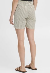 Shorts beige clair avec des rayures verticales noires ; ceinture élastique ; longueur au milieu de la cuisse ; tissu lisse ; associés à des sandales marron.