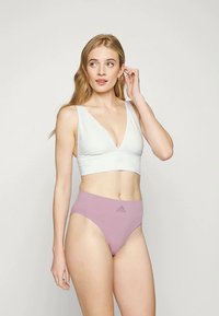 Λευκό αθλητικό σουτιέν χωρίς ραφές με βαθύ V-ντεκολτέ και ροζ ψηλόμεσο εσώρουχο που διαθέτει ανάγλυφο λογότυπο Adidas. Απαλή ύφανση, μινιμαλιστικός σχεδιασμός.