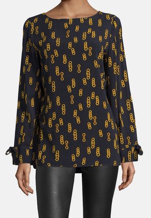 Granatowa bluzka z długim rękawem z żółtym wzorem łańcucha, okrągłym dekoltem i wiązanymi mankietami, zestawiona z czarnymi skórzanymi spodniami.