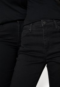 Jeans pretos com corte justo e design clássico. Apresenta bolsos frontais, fecho de botão e uma textura subtil. Estilo minimalista.