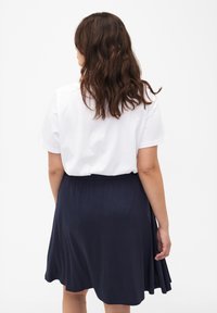 T-shirt blanc à manches courtes associé à une jupe plissée bleu marine, arrivant au genou, avec une taille élastique et une texture douce.
