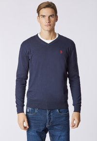 Maglione blu navy a maniche lunghe con scollo a V in tessuto morbido, caratterizzato da un piccolo logo rosso sul lato sinistro del petto e orlo e polsini a coste.