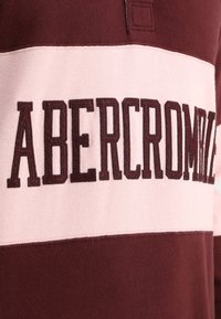 Bordeauxrode en roze gestreepte trui met geborduurd "ABERCROMBIE" in donker bordeauxrood. Voorzien van een kraag en een zachte gebreide textuur.