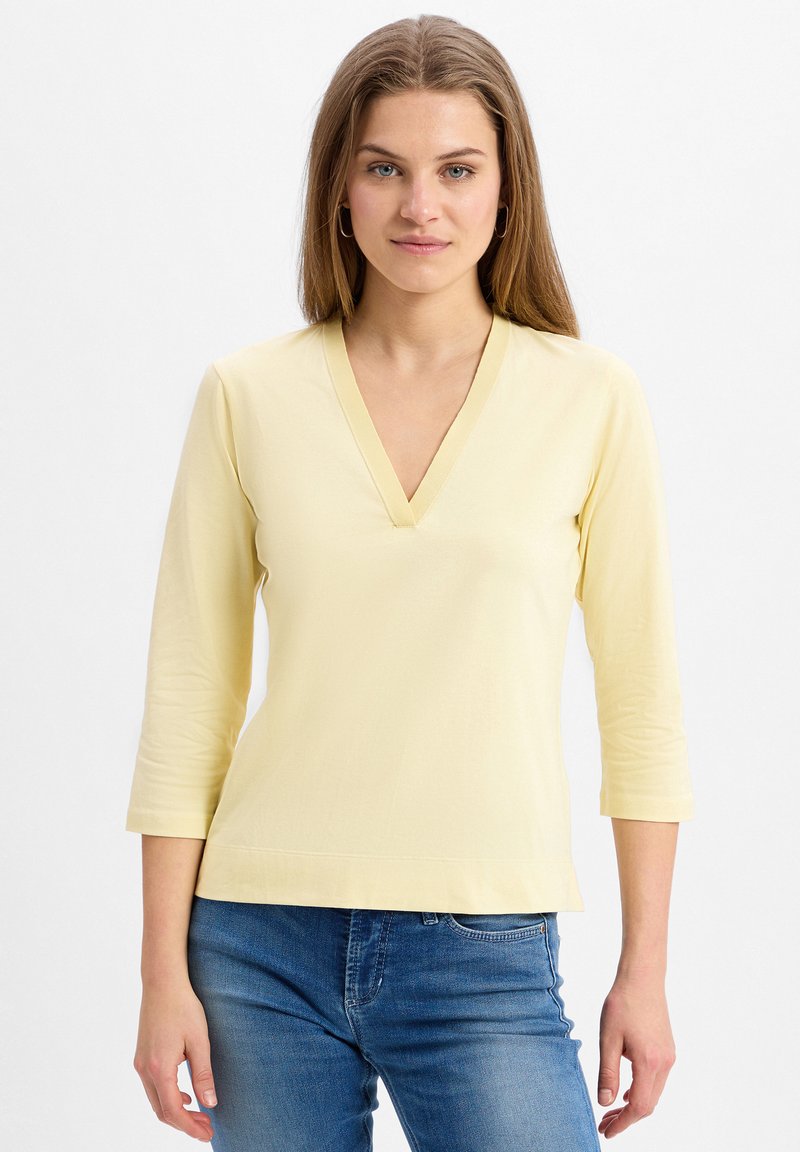 Yellow, knitted top with a V-neck and three-quarter sleeves, featuring a smooth texture and subtle stitching detail on the hem.