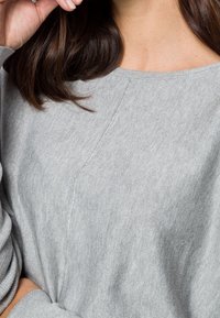 Pull en tricot gris clair avec un col rond, des poignets côtelés, et de subtils accents de couture diagonale à l'avant. Texture douce.