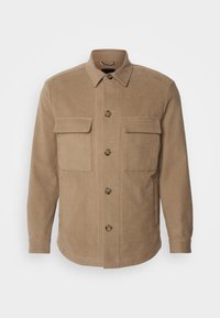 Veste chemise texturée beige avec un col, des poches poitrine et des boutons sur le devant. Fabriquée en tissu doux pour le confort.