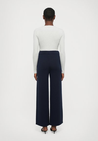 Navy wide-leg pants with a high waistband, made from textured fabric. Paired with a fitted light gray long-sleeve top.