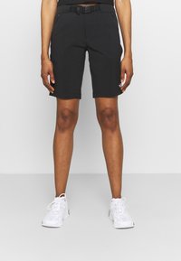 Svarta shorts med en slät textur, med en åtsittande design, bältesöglor och sidofickor med dragkedja. Matchas med vita sneakers.