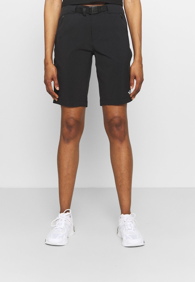 Svarta shorts med en slät textur, med en åtsittande design, bältesöglor och sidofickor med dragkedja. Matchas med vita sneakers.