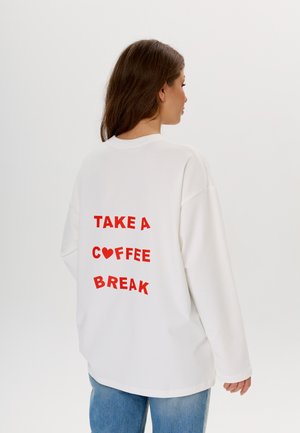 Witte oversized sweatshirt met rode tekst op de achterkant die luidt: "NEEM EEN ♥ KOFFIEPAUZE." Zacht materiaal met een comfortabele pasvorm.