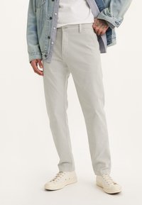 Jasnoszare bawełniane spodnie o prostym kroju, z zamkiem błyskawicznym i kieszeniami bocznymi, zestawione z off-white sportowymi butami i dżinsową kurtką.