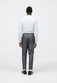 Camisa de manga comprida azul claro texturizada, calças cinzentas às riscas finas ajustadas e sapatos pretos com meias brancas. Enfoque no corte ajustado e moderno.